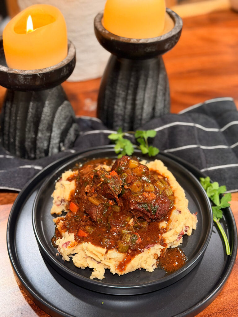 Red Wine Braised Beef w/ Garlic Mashed Potatoes - on a black serving plate with lit candles sticks in background with black and white stripes