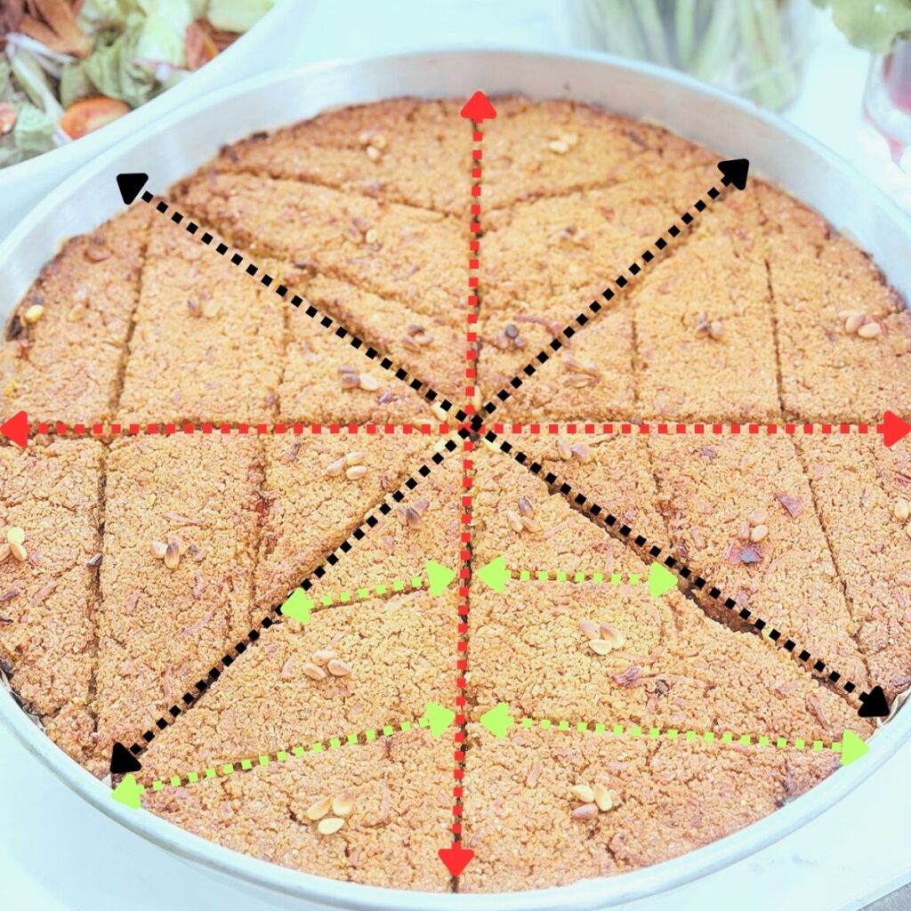 Crispy Lebanese vegan kibbeh baked in a round pan with pine nuts, served with a fresh salad and surrounded by organic vegetables like asparagus, leeks, radishes, carrots, and kale.