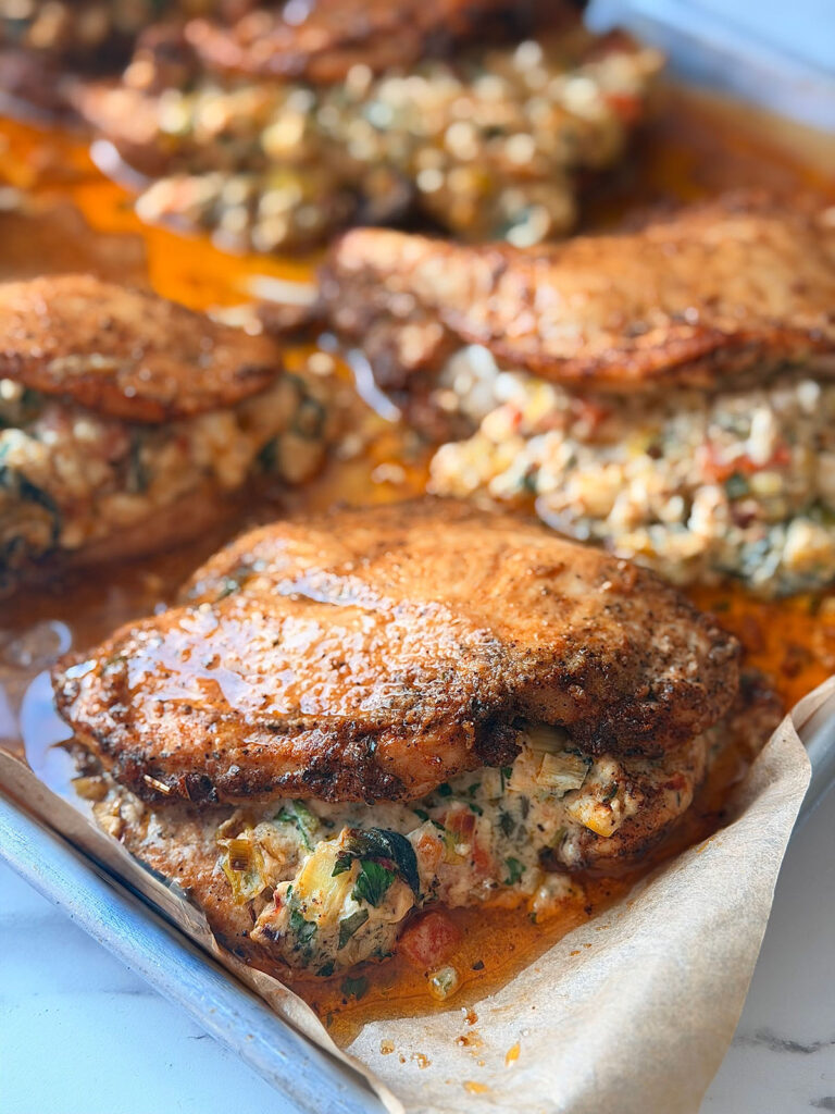 Creamy stuffed chicken filled with cottage cheese and sun-dried tomatoes. Stuffed chicken breasts are arranged on a baking sheet lined with parchment paper, resting in their own spiced juices on a white countertop.