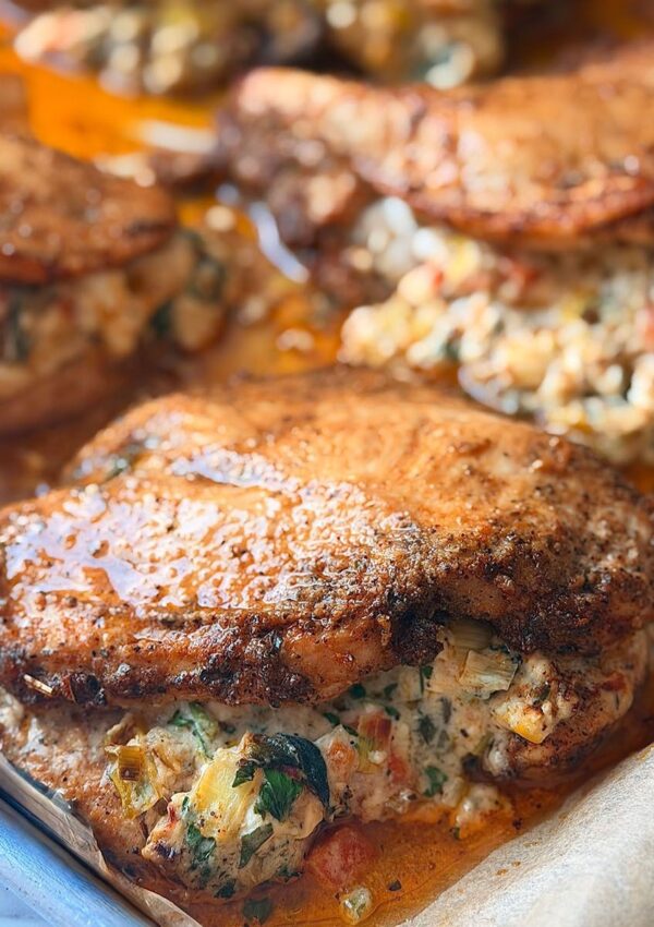 Creamy stuffed chicken filled with cottage cheese and sun-dried tomatoes. Stuffed chicken breasts are arranged on a baking sheet lined with parchment paper, resting in their own spiced juices on a white countertop.