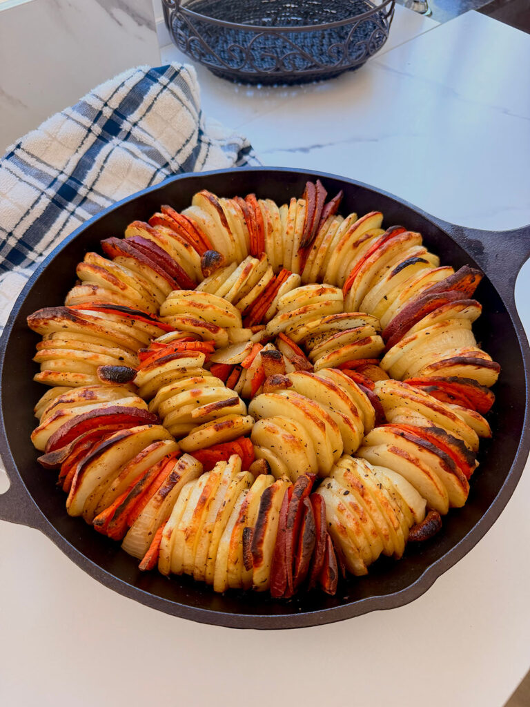 Garlic Butter Scalloped Potatoes Drizzled with Date Molasses - Mandoline potatoes in a cast-iron skillet on a white countertop with a stripped blue and white towel in background.