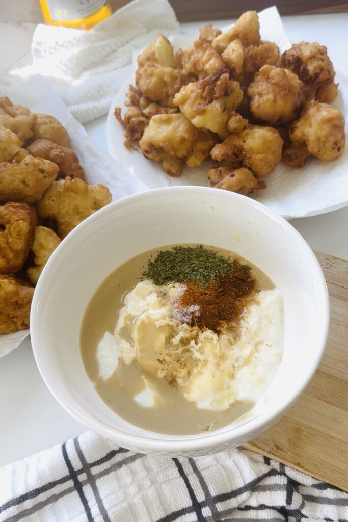Tahini Sauce - Galore Golden Sauce - Yogurt Tahini Dip perfect to pair with fries, fresh bread or fresh veggies! In a white bowl with friend cauliflower in platters surrounding the dip sauce.